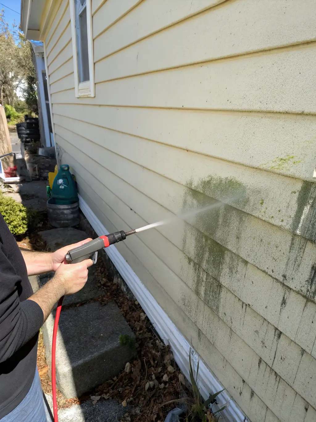 A homeowner effortlessly cleaning a section of vinyl fence with a garden hose, highlighting the ease of maintenance and time-saving benefits.
