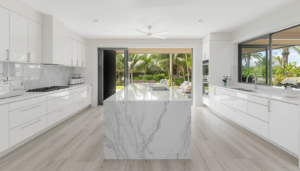 Bright-modern-Hawaiian-kitchen-with-white-cabinetry-a-quartzite-waterfall-island-light-grey-vinyl-flooring-and-an-open-view-to-a-tropical-lanai-with-lush-greenery